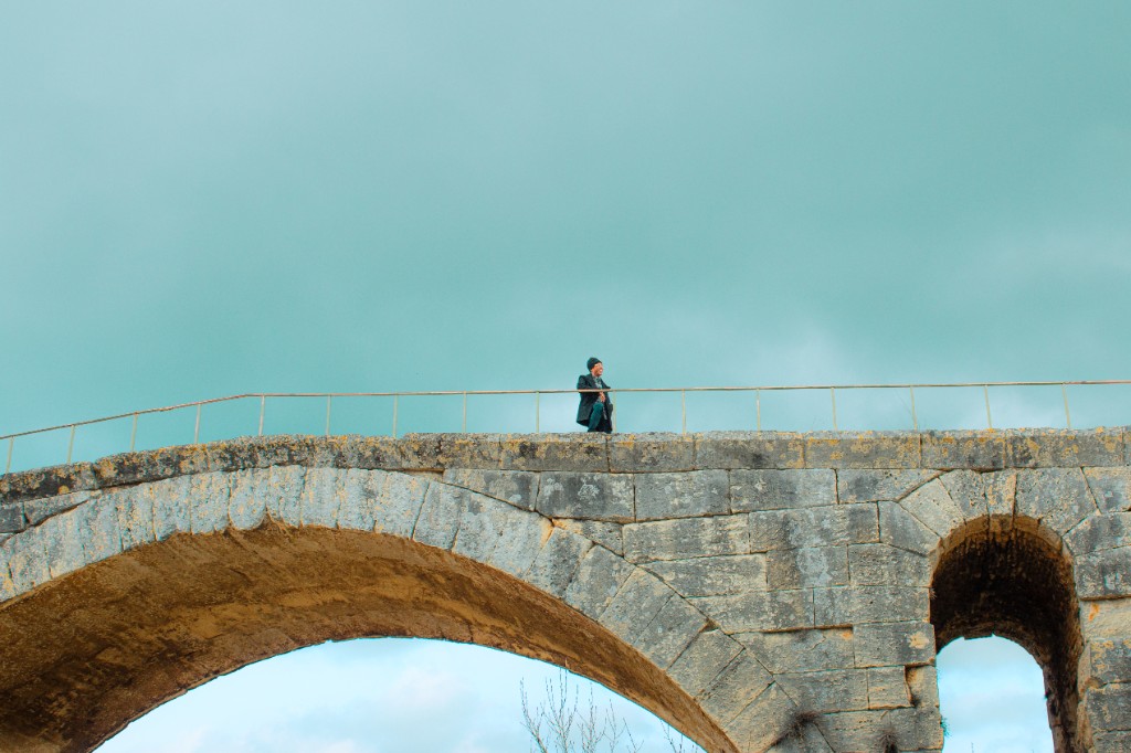 Person standing on a stone bridge against a cloudy sky